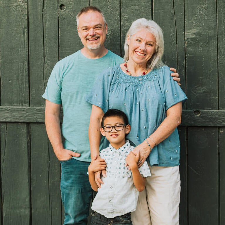 Kimberley, her husband and son smiling and posing in front of a green barn door. 