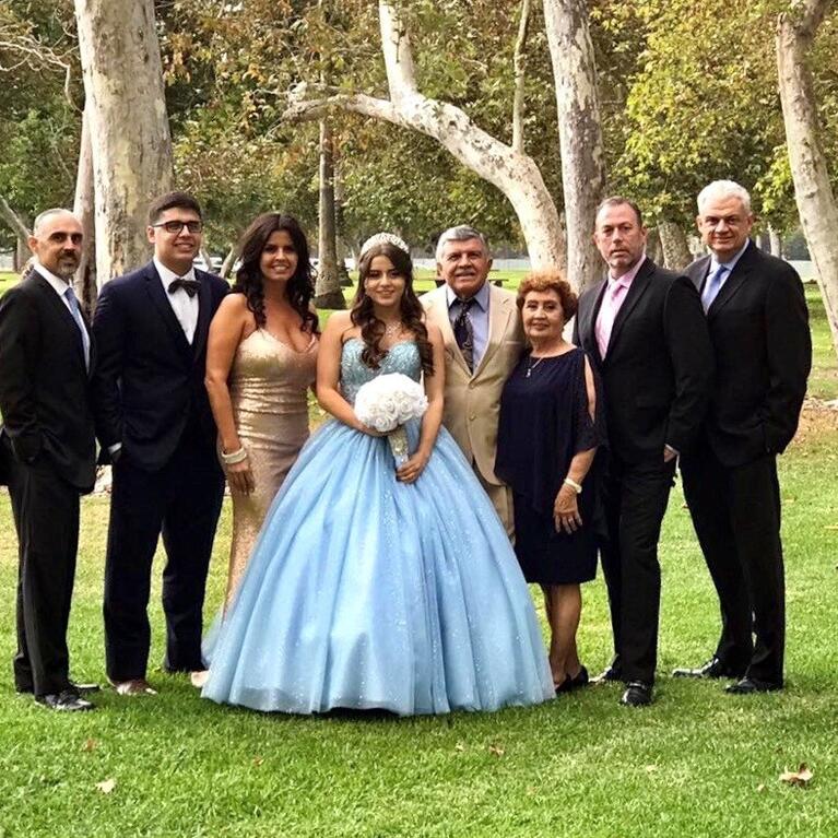 UCR's Assistant Vice Chancellor for Alumni and Constituent Relations, Jorge Ancona, far right, poses with his family during a family member's quinceañera. The celebrant is wearing a blue dress and holding a bouquet of white flowers.