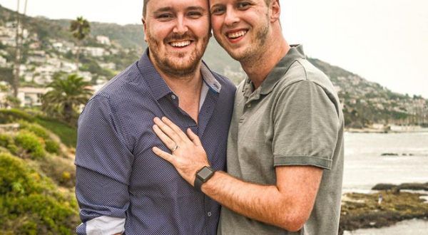 Brock Cavett, left, poses with his fiancé shortly after proposing on the cliffs of Laguna Beach, California. Brock is the Director, Programming and Career Development with Alumni Engagement. Brock is wearing a dark button-down shirt, while his fiancé wears a light polo shirt and has his hands on Brock's chest. The coast and shoreline of Laguna Beach is behind them.