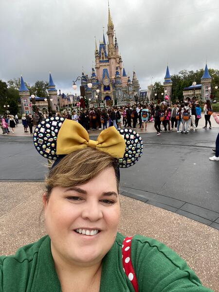 Heather Morales smiles while wearing Minnie Mouse ears in front of the Disneyland Castle on a cloudy day