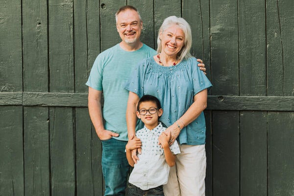 Kimberley, her husband and son smiling and posing in front of a green barn door. 