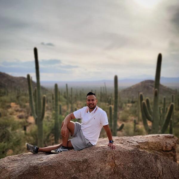 Melbert Sebayan, an enrollment marketing manager with University Communications, is wearing a white polo with the gay pride colors on the collar, poses on a rock in Saguaro National Park, outside Tucson, Arizona