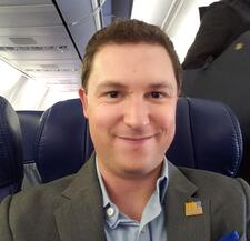 Elliot Emmer, Senior Associate Director of Development, BCOE, gives a warm grin while he sits on an airplane. He is wearing a gray sports jacket with a UCR lapel pin.