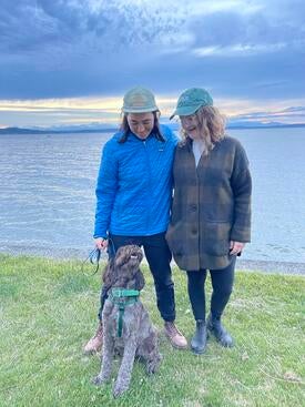 Advancement Allies - Monique Dozier Kelly Kraus Lee, Director of Development, Education and Policy posses with her wife and dog near a lake on a camping roadtrip.