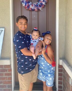 DuBron Rabb's 3 children, Isaiah, Eliza and Leilah pose together in front of their home door wearing festive July 4th outfits. 