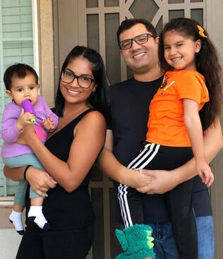 Melissa, her husband and two children smile and pose in front of their home. 